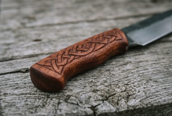 Viking seax knife close up of the engraved rosewood handle with carved knotwork pattern on a weathered plank