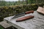 Viking seax knife with engraved rosewood handle lying on a wooden table next to its wooden blade cover