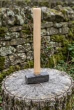 Viking style hammer standing upright on a tree stump, ash wood handle rising in front of a dry stone wall
