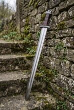 Hand forged steel Viking sword standing upright against an old mossy stone wall on stone steps, full length in view