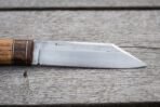 High carbon steel seax knife blade in close view beside a wood handle with dark bolster and brass spacer on grey boards