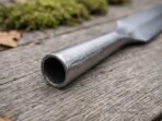 Hollow steel socket of a hand forged spear head shown close up on weathered wood with moss and oak leaves behind
