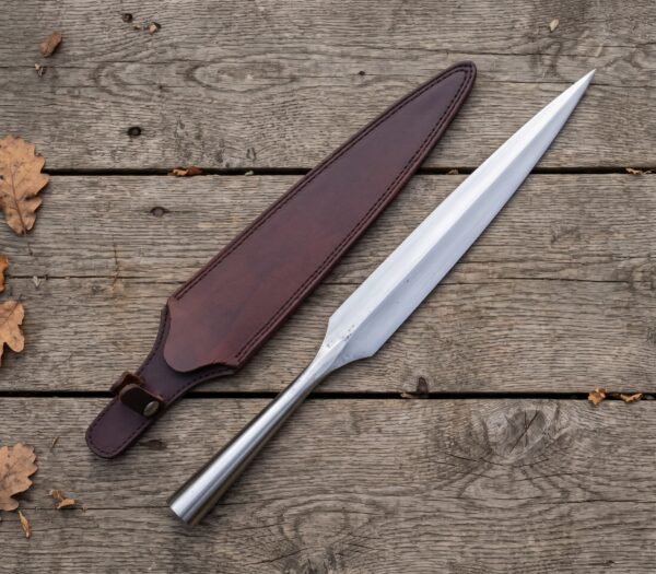Polished steel spear head with long leaf shaped blade and hollow socket lying beside its dark brown leather sheath on wood