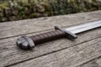 Viking sword hilt in close view, leather wrapped steel grip with crossguard and rounded pommel on a weathered table
