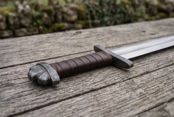 Viking sword hilt in close view, leather wrapped steel grip with crossguard and rounded pommel on a weathered table