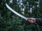 Curved stainless steel elven sword with etched script on the blade held up in one hand in front of a dark forest