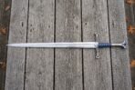 Full length stainless steel fantasy longsword with blue grip and silver fittings laid across grey decking with oak leaves
