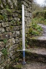 Stainless steel fantasy longsword standing point up against a mossy dry stone wall beside garden steps
