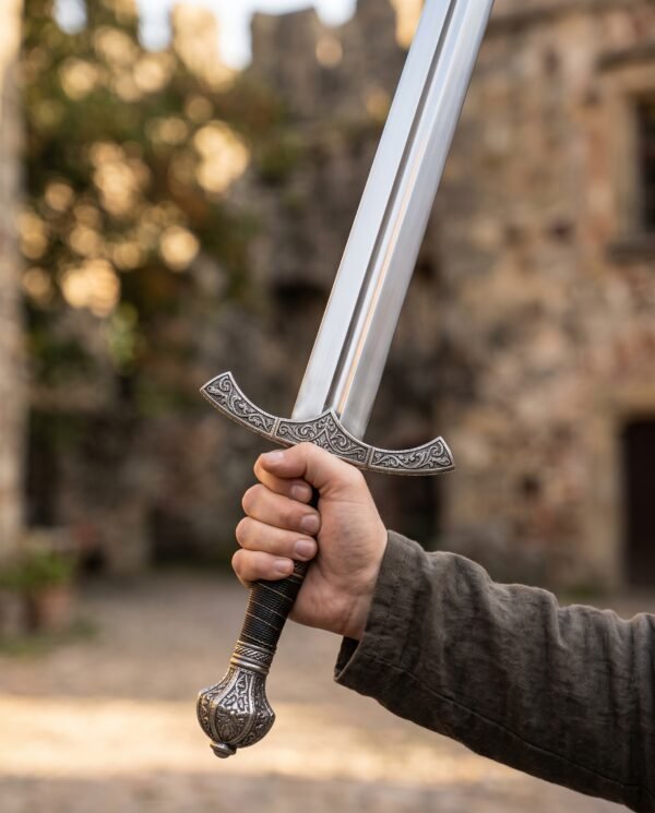 Stainless steel fantasy sword raised upright in one hand, showing the engraved guard and pommel in a castle courtyard