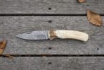 Damascus folding knife with camel bone handle and stag bolster lying open on grey wooden boards, full side view
