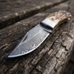 Damascus steel folding knife with stag horn handle, close up of the blade pattern and steel bolster on weathered wood