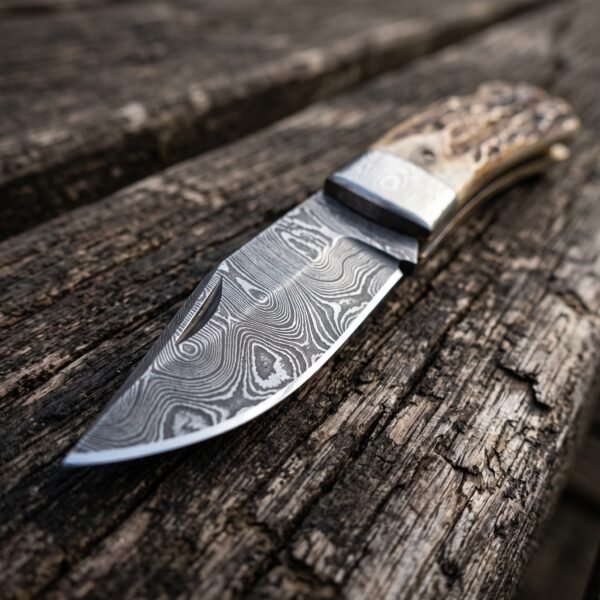 Damascus steel folding knife with stag horn handle, close up of the blade pattern and steel bolster on weathered wood