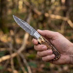 Damascus steel folding pocket knife with stag horn handle held open in a hand against blurred autumn woodland