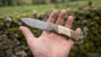 Damascus steel folding pocket knife with ram horn, bone and honeycomb handle lying open across an outstretched palm