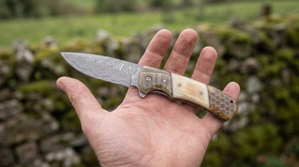 Damascus steel folding pocket knife with ram horn, bone and honeycomb handle lying open across an outstretched palm