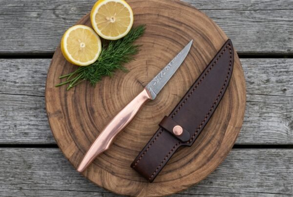 Damascus fillet knife with copper handle on a round wooden board with lemon halves, dill and a dark leather sheath