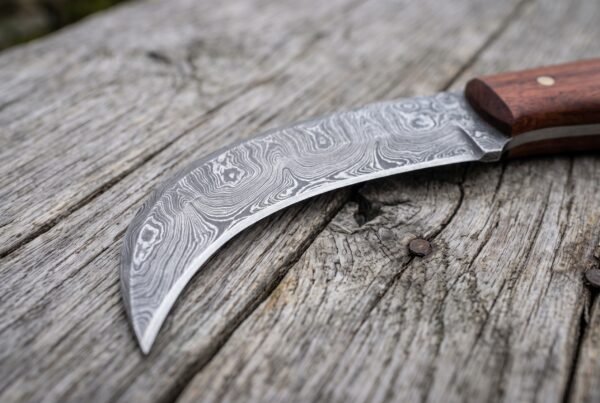 Close view of the curved Damascus steel blade showing its swirling pattern and sharp hooked tip on a grey wooden surface