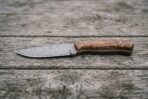 Skinner knife with wood handle lying flat on grey weathered planks, full side view of the blade and handle