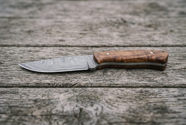 Skinner knife with wood handle lying flat on grey weathered planks, full side view of the blade and handle