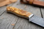 Damascus camp knife close up of the olive wood handle grain and steel bolster with the patterned blade