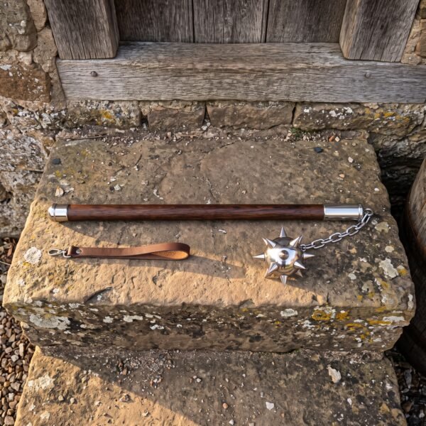 Hand forged medieval flail with a polished steel spiked ball on a chain and a walnut haft lying on a weathered stone step below a timber door