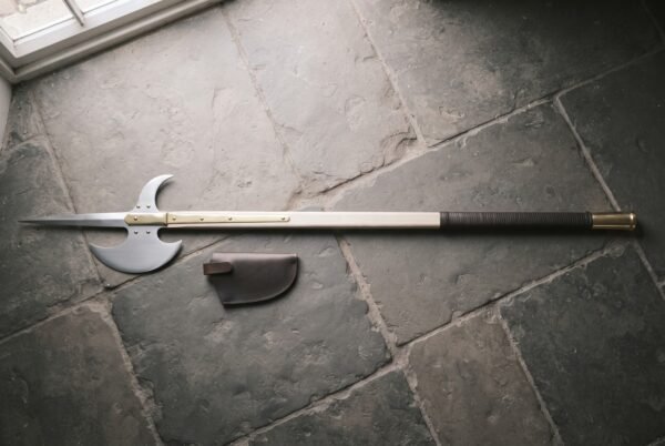 Hand forged halberd with a polished steel spike, crescent blade and rear fluke on an ash haft with brass langets lying on grey flagstones by a leather cover