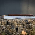 Hand forged Viking sword in polished high carbon steel with brown leather scabbard and brazil nut pommel, laid across a low drystone wall in daylight