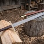 Hand forged Damascus sword with a layered fullered double edged blade and large disc pommel resting on a split log and tree stump in a timber yard