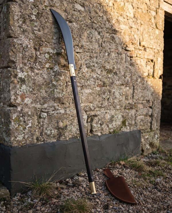 Medieval glaive with a long blackened curved steel blade and brass langets on a dark haft leaning against a rough limestone barn wall on gravel
