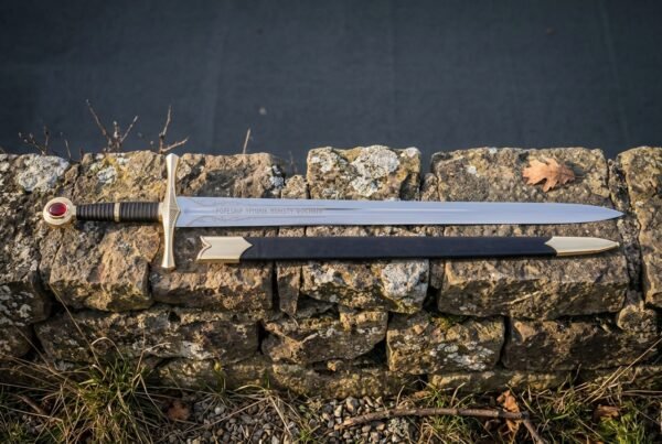Hand forged runic sword with a darkened Elder Futhark blade inscription, deep red leather grip and steel disc pommel lying on a dark drystone wall