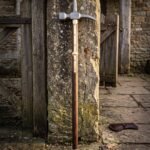 Hand forged medieval polehammer with a steel hammer head and top spike on a walnut haft with brass langets leaning against a weathered stone pier
