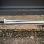 Hand forged Carolingian sword with polished fullered blade, long straight crossguard and brown leather scabbard resting on a weathered stone doorstep