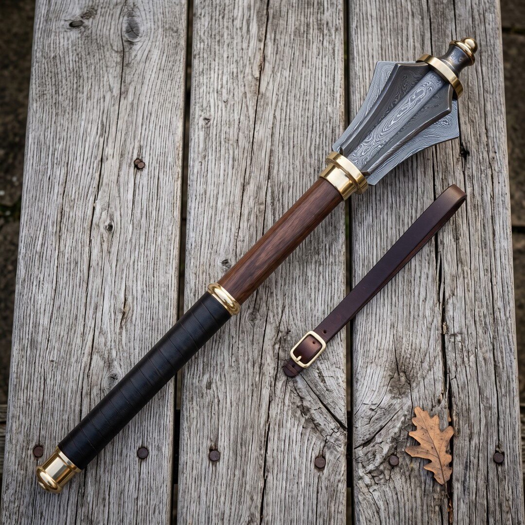 Gemini_Generated_Image_h835lgh835lgh835 Damascus mace with six forge welded flanges, brass collars and a rosewood haft lying on a silvered timber table beside a buckled leather wrist strap