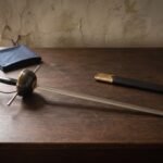 Hand forged musketeer sword with a blackened cup hilt and polished brass rim resting on a dark oak table beside a blue cloth and its black leather scabbard