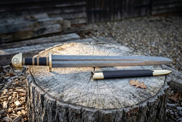 Damascus Viking sword with dark etched layered steel blade and black leather scabbard resting on a weathered tree stump in a wooded clearing