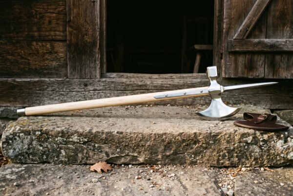 Hand forged poleaxe with a polished steel crescent blade, hammer poll and spike on a pale ash haft lying across a stone doorstep beside a leather head cover
