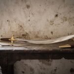 Hand forged Indian talwar with a deeply curved polished blade, rosewood grip and solid brass knuckle guard resting on a dark timber table against a pale plaster wall