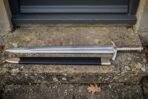 Elven sword replica with an engraved double edged blade and black leather scabbard resting on a weathered stone doorstep outside a stone cottage