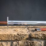 Hand forged medieval falchion with a broad straight backed polished blade and rosewood grip lying on a sandstone ledge beside a red leather scabbard