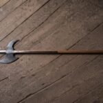 Battle halberd with a satin steel spike, crescent blade and hooked fluke on a long hardwood haft laid across a dark weathered plank floor