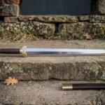 Hand forged Chinese jian sword with a straight polished double edged blade and brass ferruled grip resting on a sandstone step below a dry stone wall