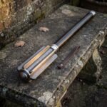 Damascus bar mace with a deeply fluted forge welded head and blackened steel haft resting on a weathered stone garden bench with fallen leaves