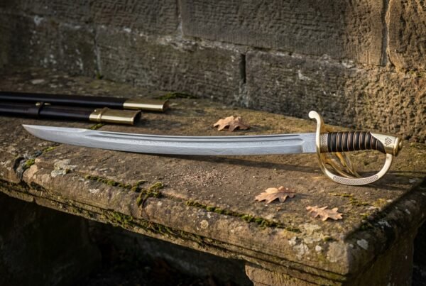 Hand forged Damascus sabre with a layered curved blade, ornate three bar brass hilt and brass wired leather grip lying on a mossy stone garden bench beside its black leather scabbard
