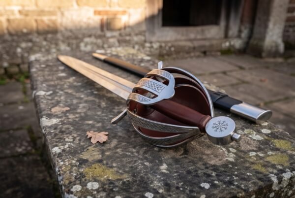 Basket hilt sword lying diagonally on a lichen covered stone bench with its dark leather scabbard behind it