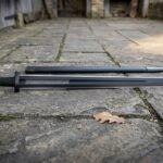 Black Damascus Viking sword with dark etched layered blade and an inscription across the face, resting on grey flagstone paving beside its black scabbard
