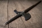 Blackened steel halberd head with riveted langets and a broad axe blade lying at an angle on worn wooden planks