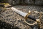 Close up of the knotwork cut brass knuckle bow, ribbed black leather grip and brass pommel of a Damascus steel cutlass