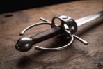 Close up of the polished ring and shell guard, brown leather grip and round pommel of a steel fencing sword
