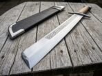 Close view of a grosse messer blade with etched knotwork band and clipped tip, steel cross guard and black sheath on old boards