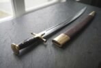 Close view of a talwar brass disc pommel and cross guard with the curved blade and leather scabbard on dark slate